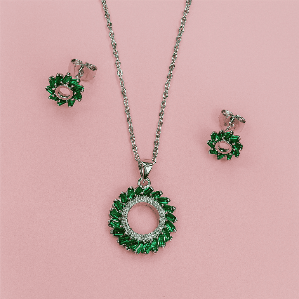 Elegant emerald green halo pendant necklace and stud earrings set displayed on pink background