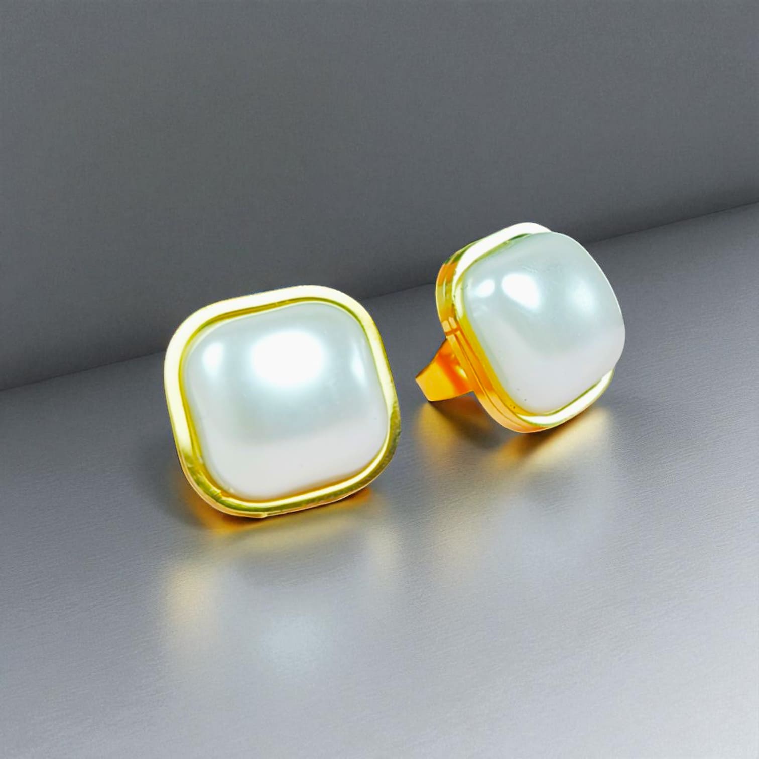 Square pearl stud earrings with gold-plated frames displayed on gray surface