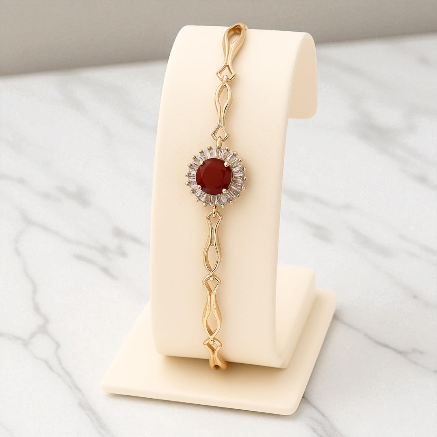 Gold-tone bracelet with red gemstone and zircon accents on beige stand against marble background