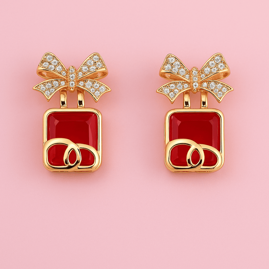 Gold bow-shaped earrings with red square stones and zircon accents on pink background