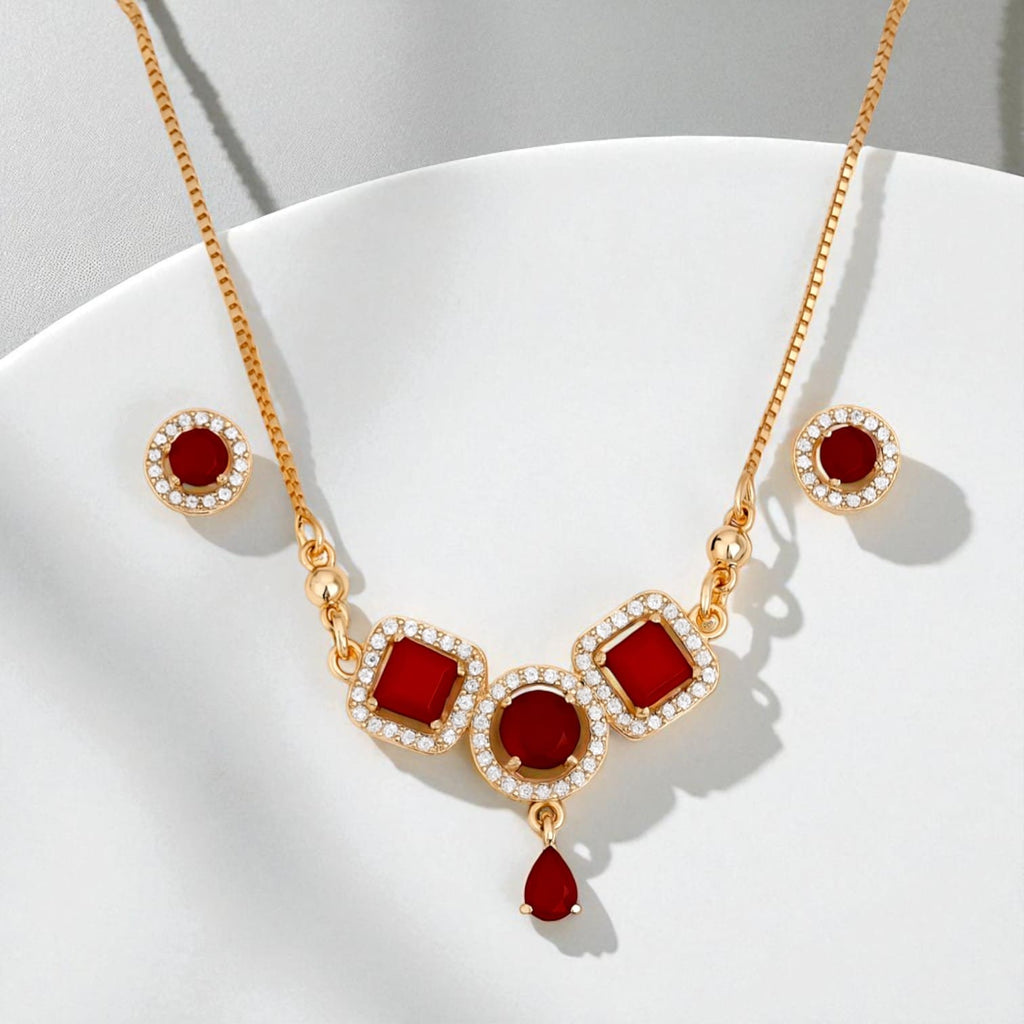 Gold necklace and earrings set with red stones and zircon accents displayed on white surface